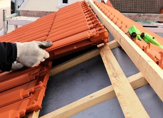 Couvreur remplaçant des tuiles en terre cuite sur une toiture près de Clisson